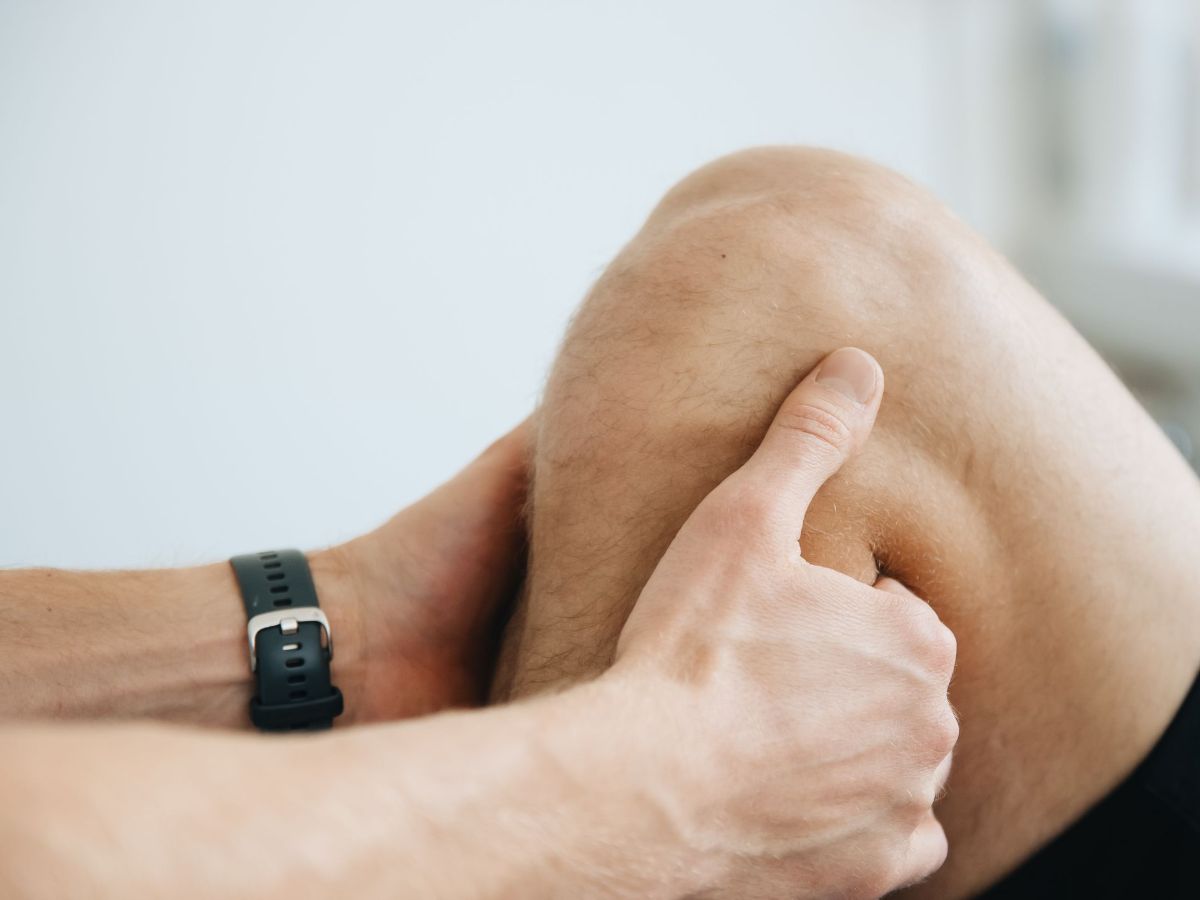 A physiotherapist's hands examining a patient's bent knee, pressing gently around the joint