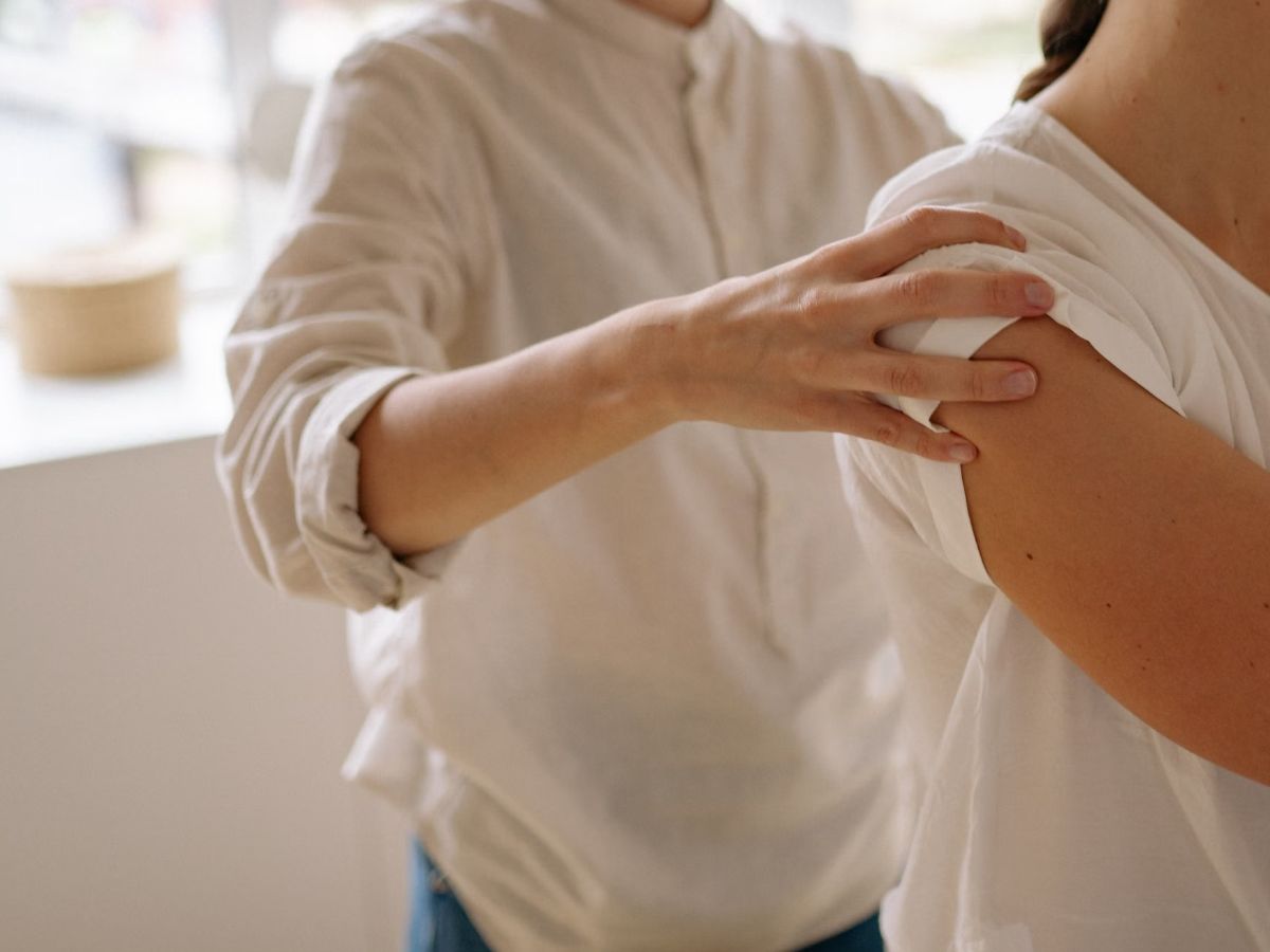 A physiotherapist's hands supporting a patient's shoulder during an assessment